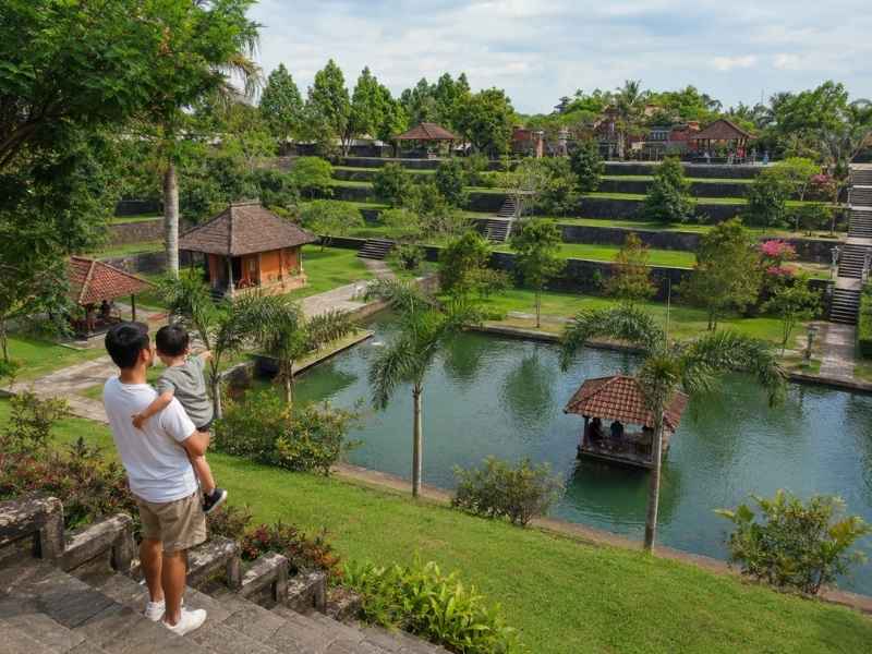 Ayah dan anak melihat kolam serta taman hijau dari area tangga Taman Narmada