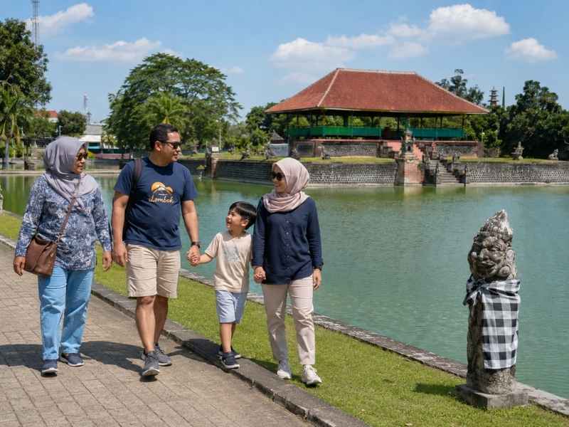 Keluarga berjalan santai di tepi kolam Taman Mayura Lombok