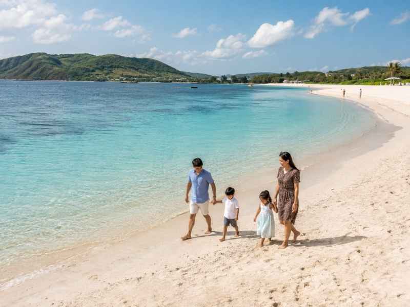 Keluarga berjalan santai di Pantai Kuta Mandalika dengan laut biru dan perbukitan Lombok